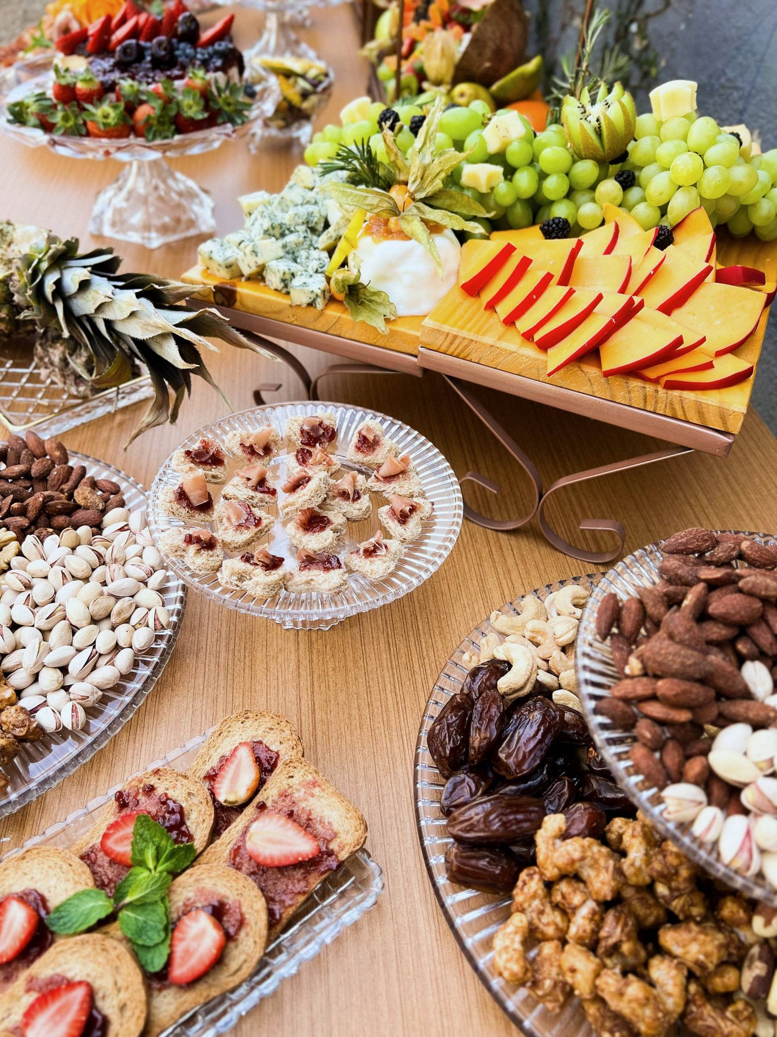 Vista de cima da mesa: castanhas, tâmaras, canapés, queijos, uvas e torradas com morango.